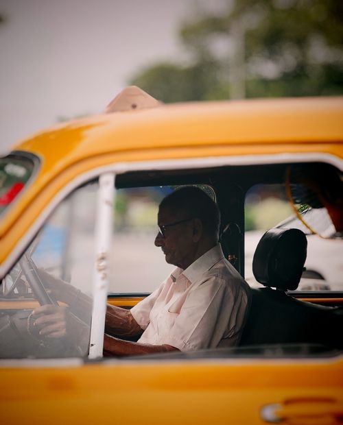 Free An elderly man drives a classic yellow taxi in the bustling streets of Kolkata, showcasing local transportation culture. Stock Photo