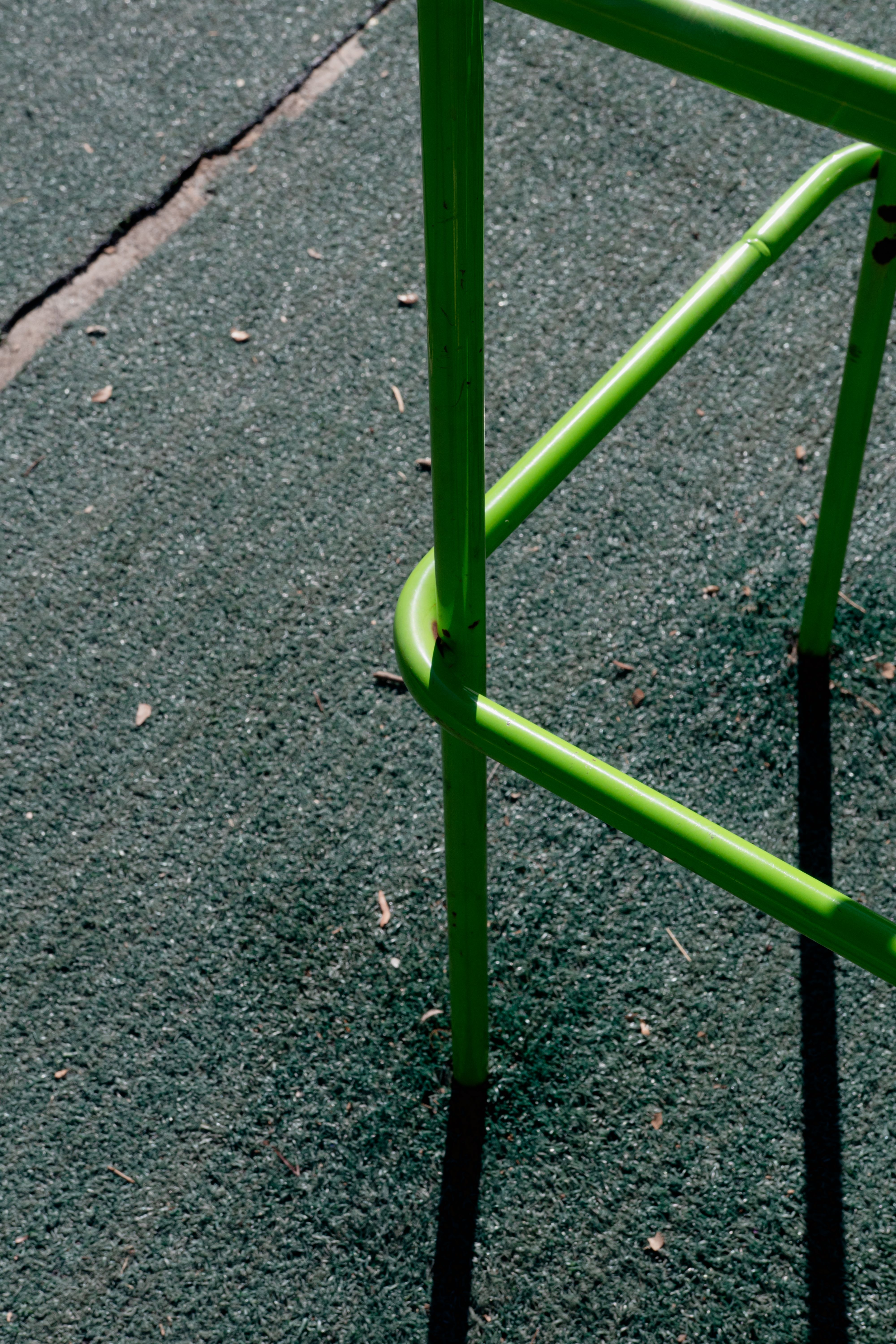 Close-up of a vibrant green metal chair leg on a textured outdoor surface, creating a minimalist and modern look.
