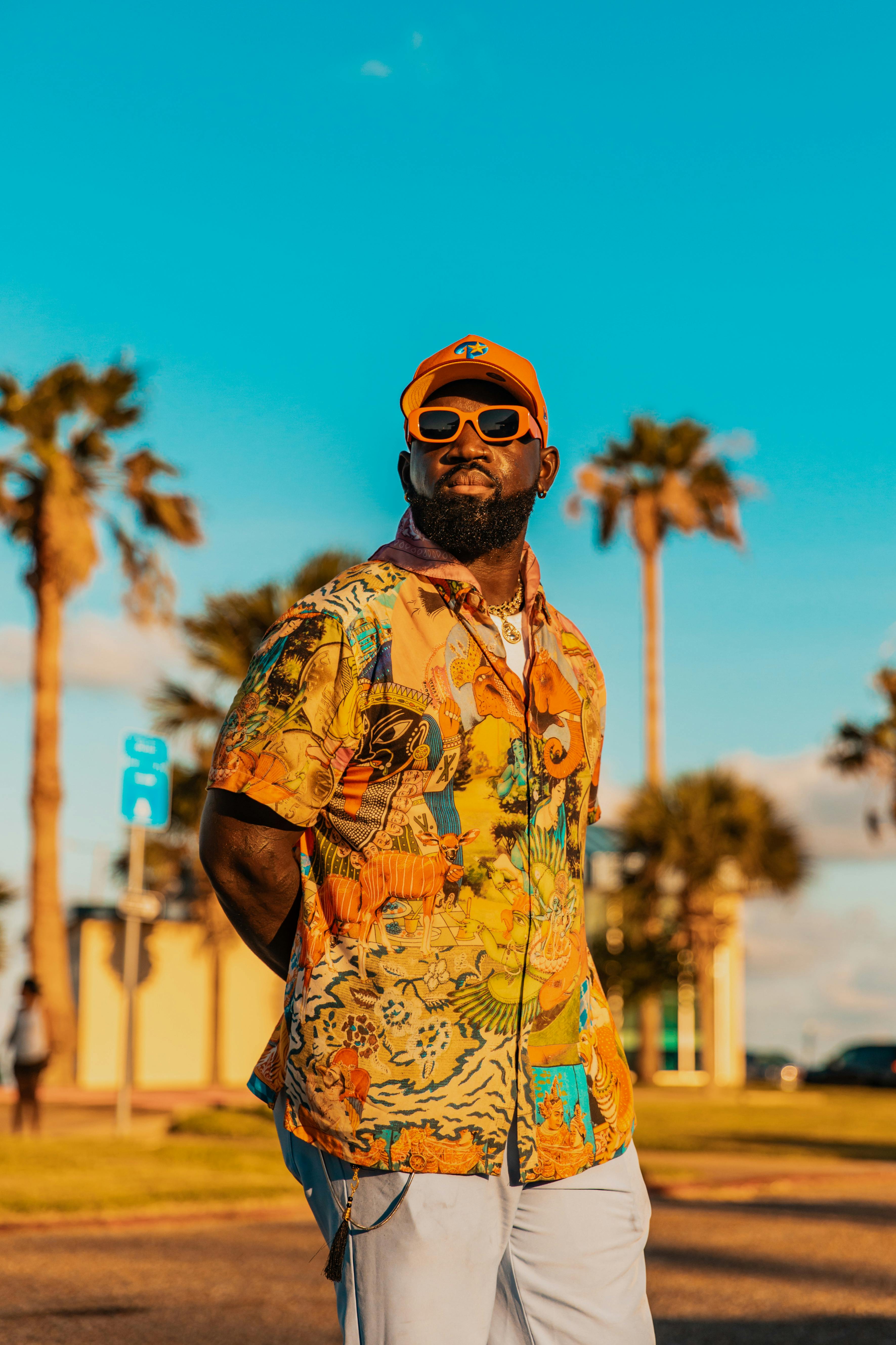 Stylish man in vibrant shirt poses against palm trees during sunset, exuding summer vibes.