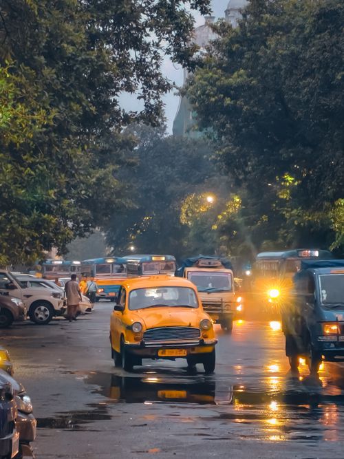 Free A bustling urban street with a classic yellow taxi amidst traffic at dusk, showcasing vibrant city life. Stock Photo