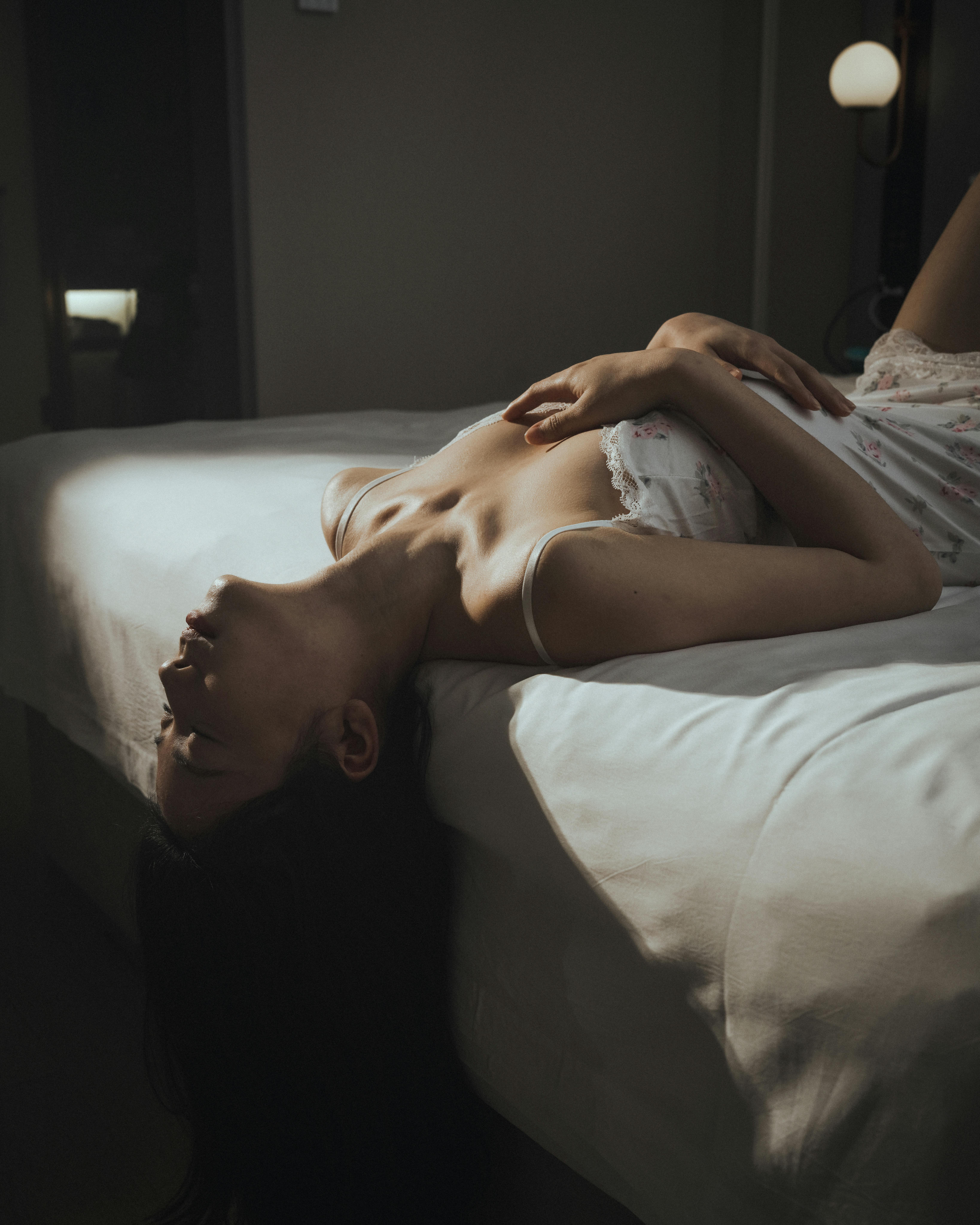Dreamy woman relaxing on bed in dimly lit room, body soft and surrendered, embodying the post-first-climax deepening phase