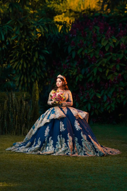 Free A woman in a luxurious, embroidered gown holds flowers in a lush garden. Stock Photo