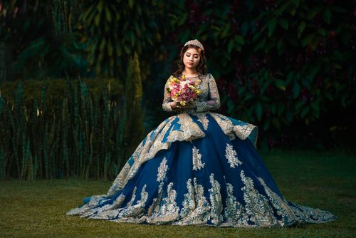 Free A woman in a stunning blue gown holds flowers in a lush garden setting. Perfect for fairytale and formal themes. Stock Photo