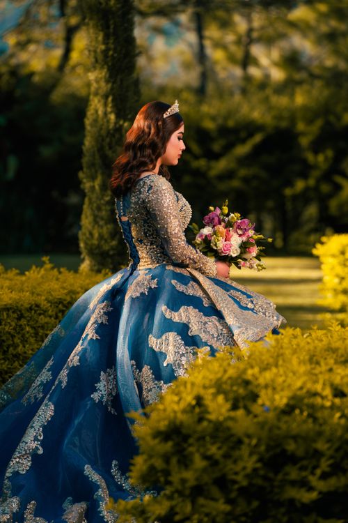 Free A woman in a luxurious blue gown with floral bouquet outdoors. Stock Photo