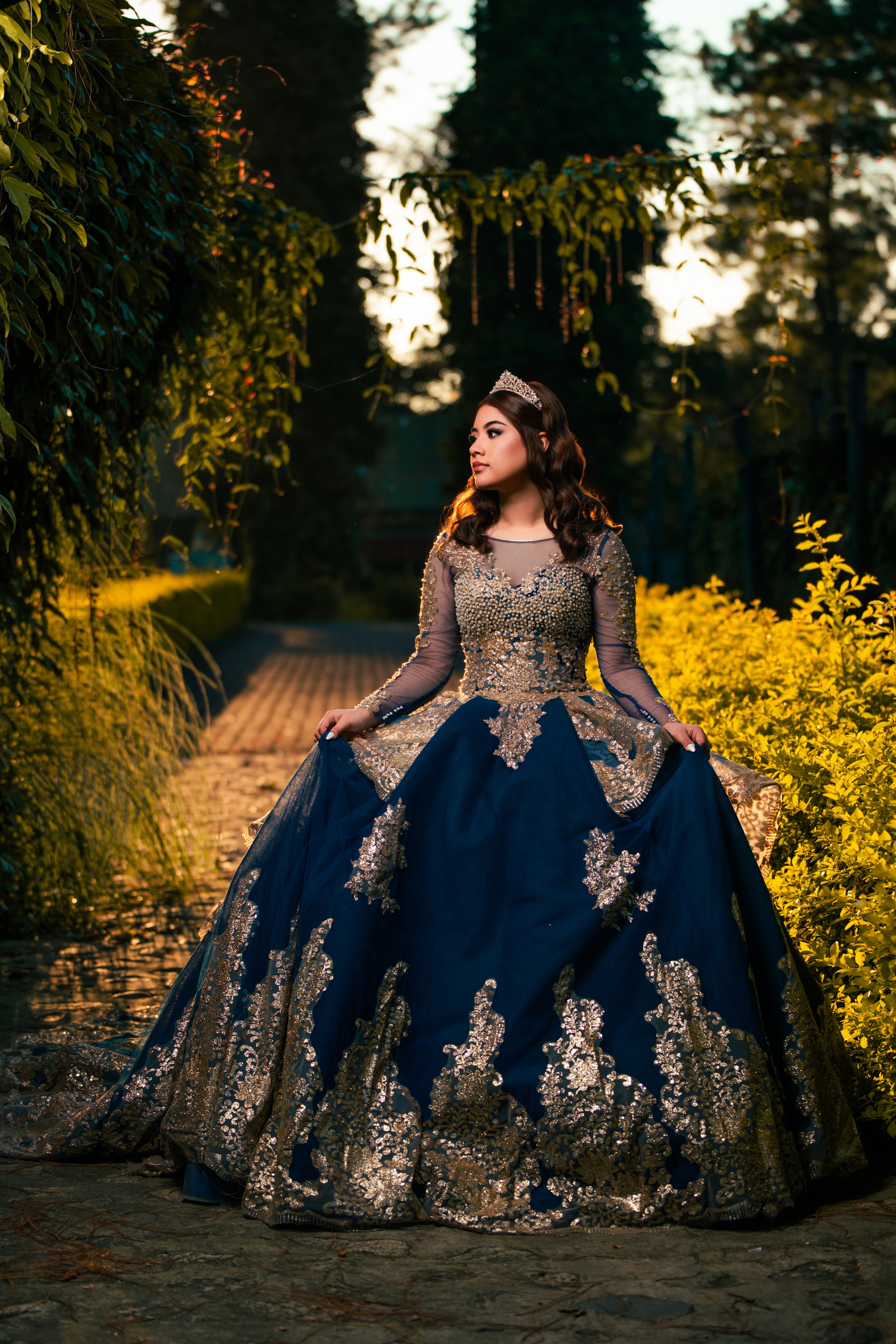 A woman in a luxurious royal blue gown stands gracefully in an enchanting garden.