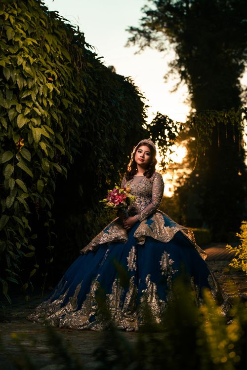 Free A woman in a detailed evening gown stands in a garden at sunset holding a bouquet. Stock Photo