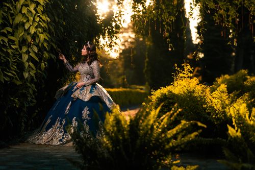 Free A woman in a blue and silver gown amidst lush greenery during sunset, creating a magical atmosphere. Stock Photo