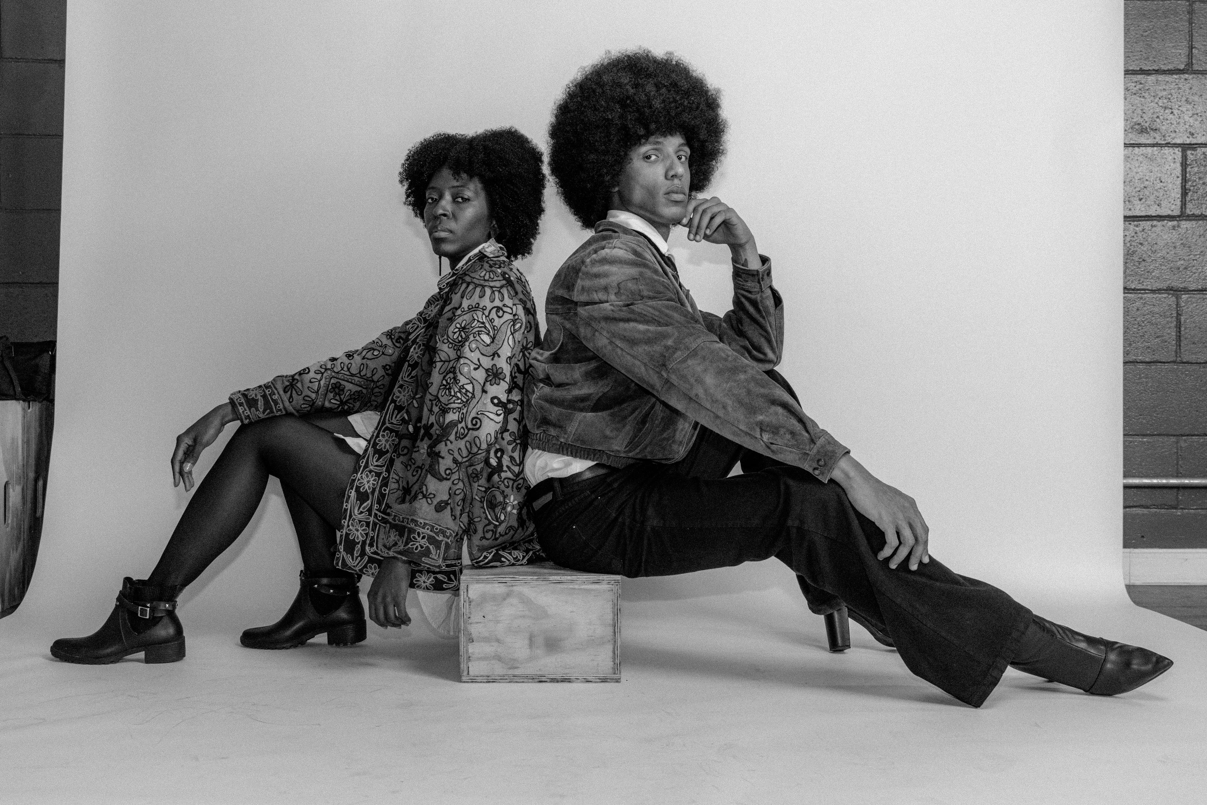 Black and white portrait of two stylish models sitting back to back in São Paulo studio.