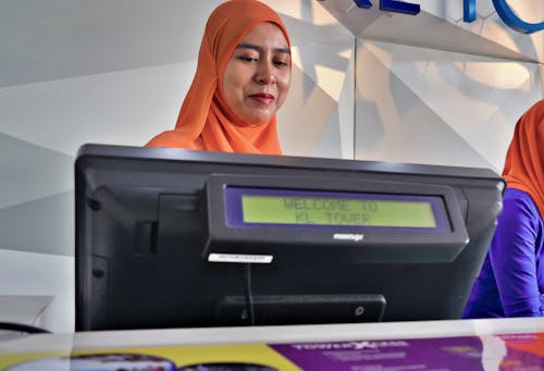 Woman in Orange Hijab Standing Near Black Digital Device