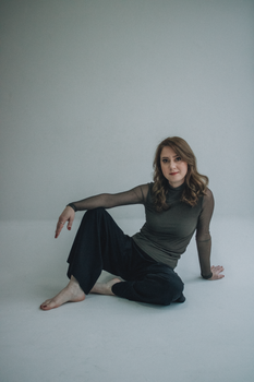 A woman seated comfortably on the floor in a minimalist studio setting.