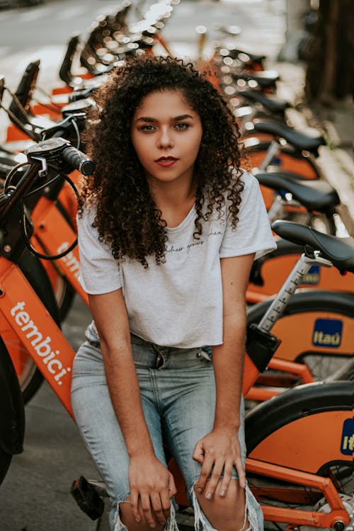 Free Woman Wearing White Shirt and Blue Denim Jeans Standing Near Bicycles Stock Photo