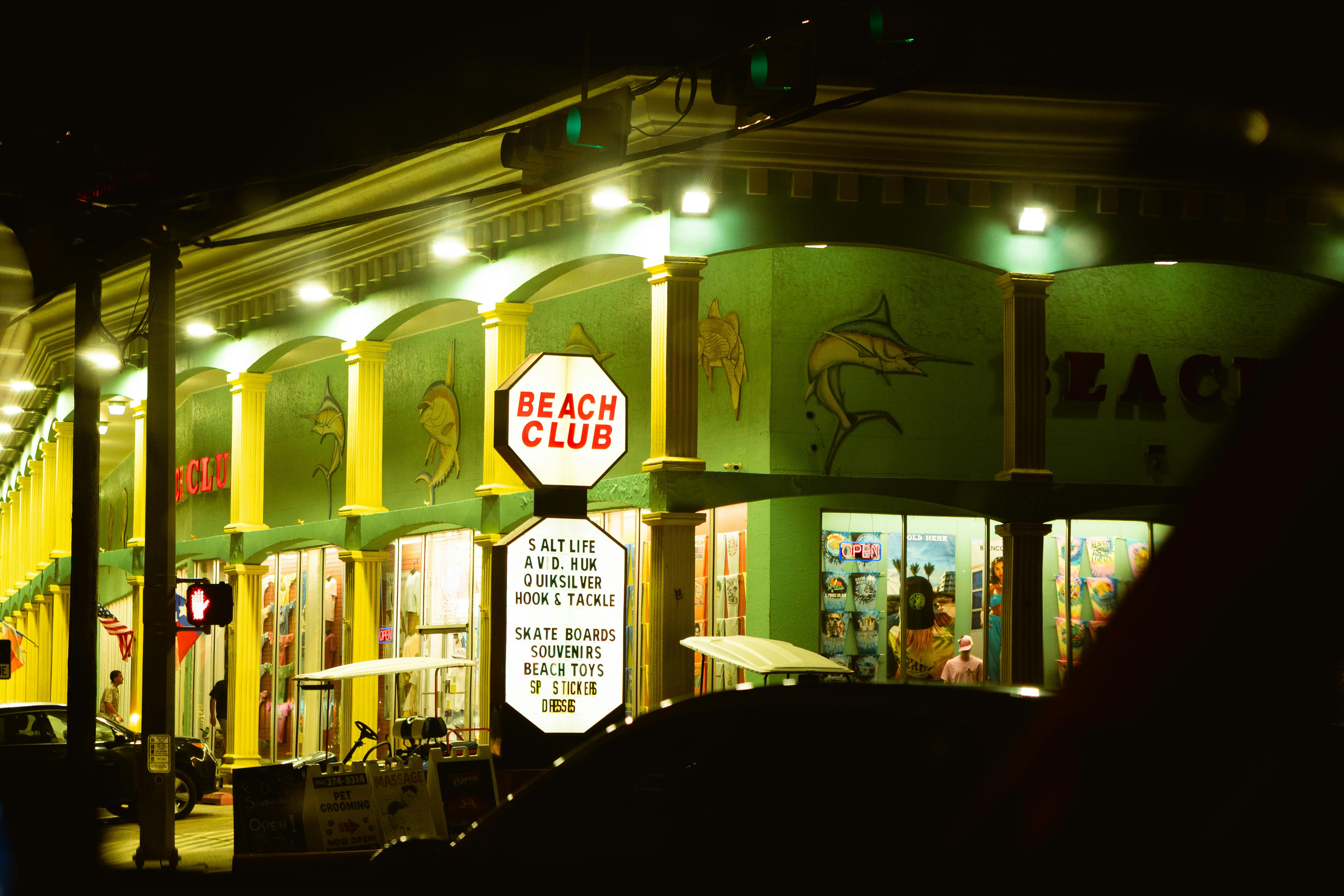 Illuminated Beach Club storefront on Padre Island at night, featuring colorful signage and vibrant decor.
