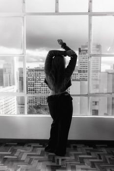 Silhouette of a woman looking out a city window, embracing urban serenity.