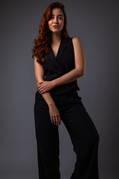 Confident red-haired woman poses gracefully in black attire against dark background.
