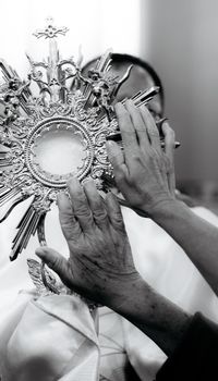 A monochrome photo showing hands touching an ornate religious monstrance, suggesting faith.