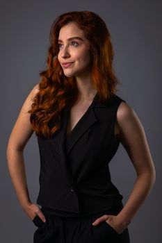 Elegant portrait of a red-haired woman in a stylish black outfit against a neutral background.
