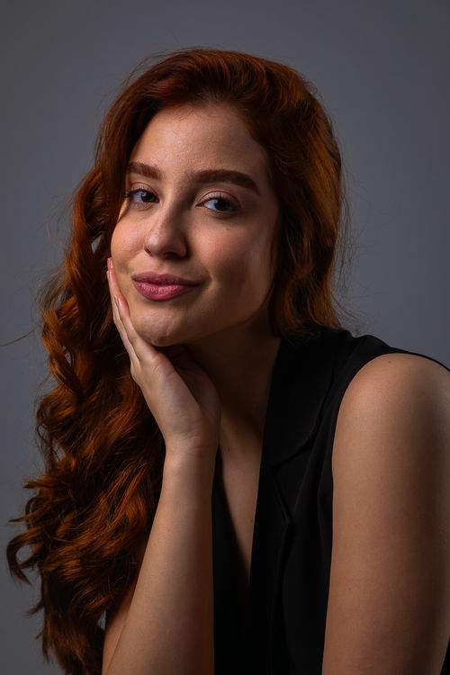 Free Close-up portrait of a woman with red curly hair in a thoughtful pose against a gray background. Stock Photo