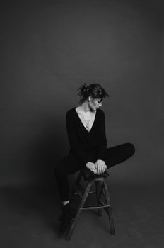 Stylish black and white portrait of an elegant woman gracefully posing on a stool.