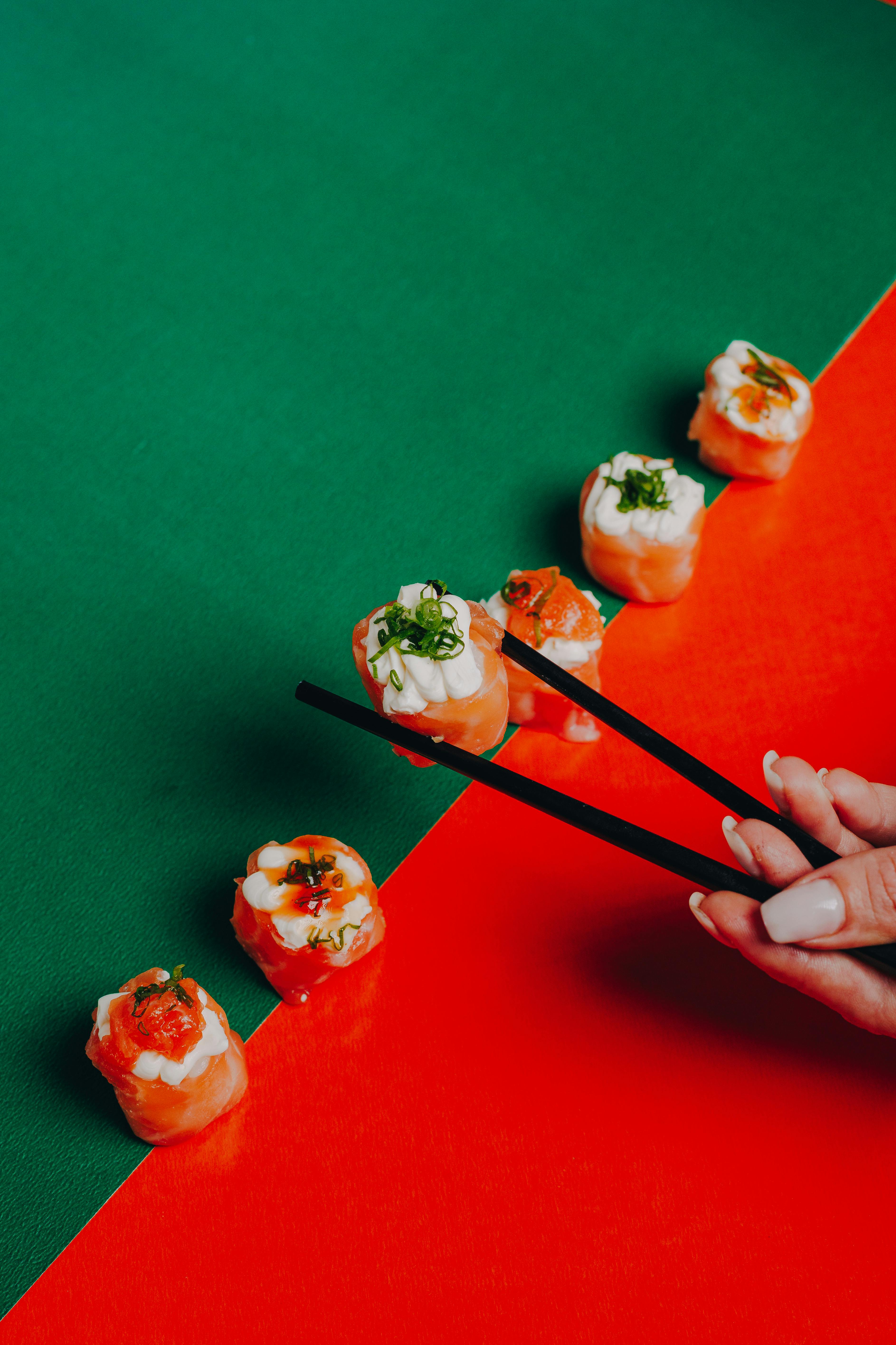 Colorful sushi rolls on vibrant background with a hand using chopsticks.