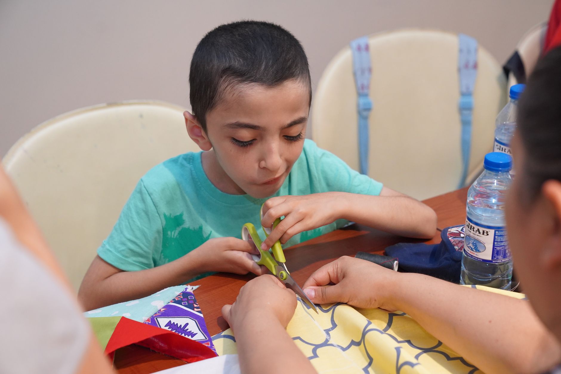 school iftar event organizer — A child focused on crafting with scissors and colorful papers during an indoor arts and crafts