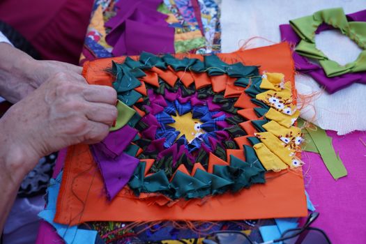 Vibrant patchwork art being crafted by hands on a worktable.