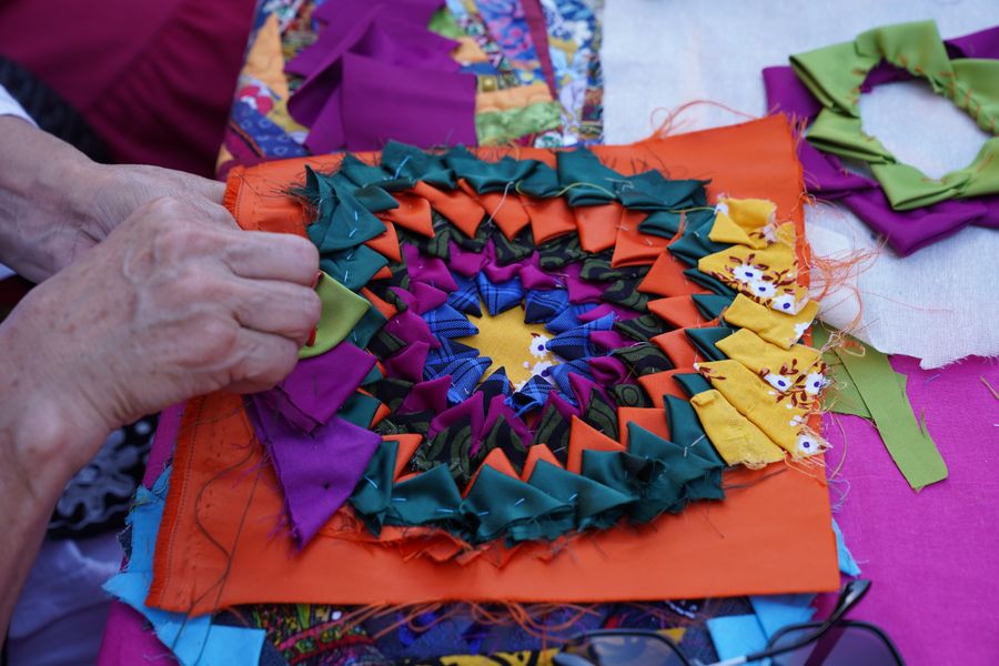 Hands arranging colorful patchwork fabric pieces into an artwork on a worktable