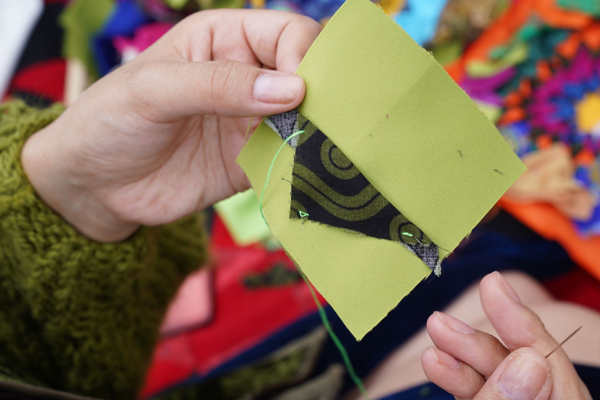 Close-up image of hands quilting with vibrant fabrics and intricate patterns, showcasing traditional sewing techniques.