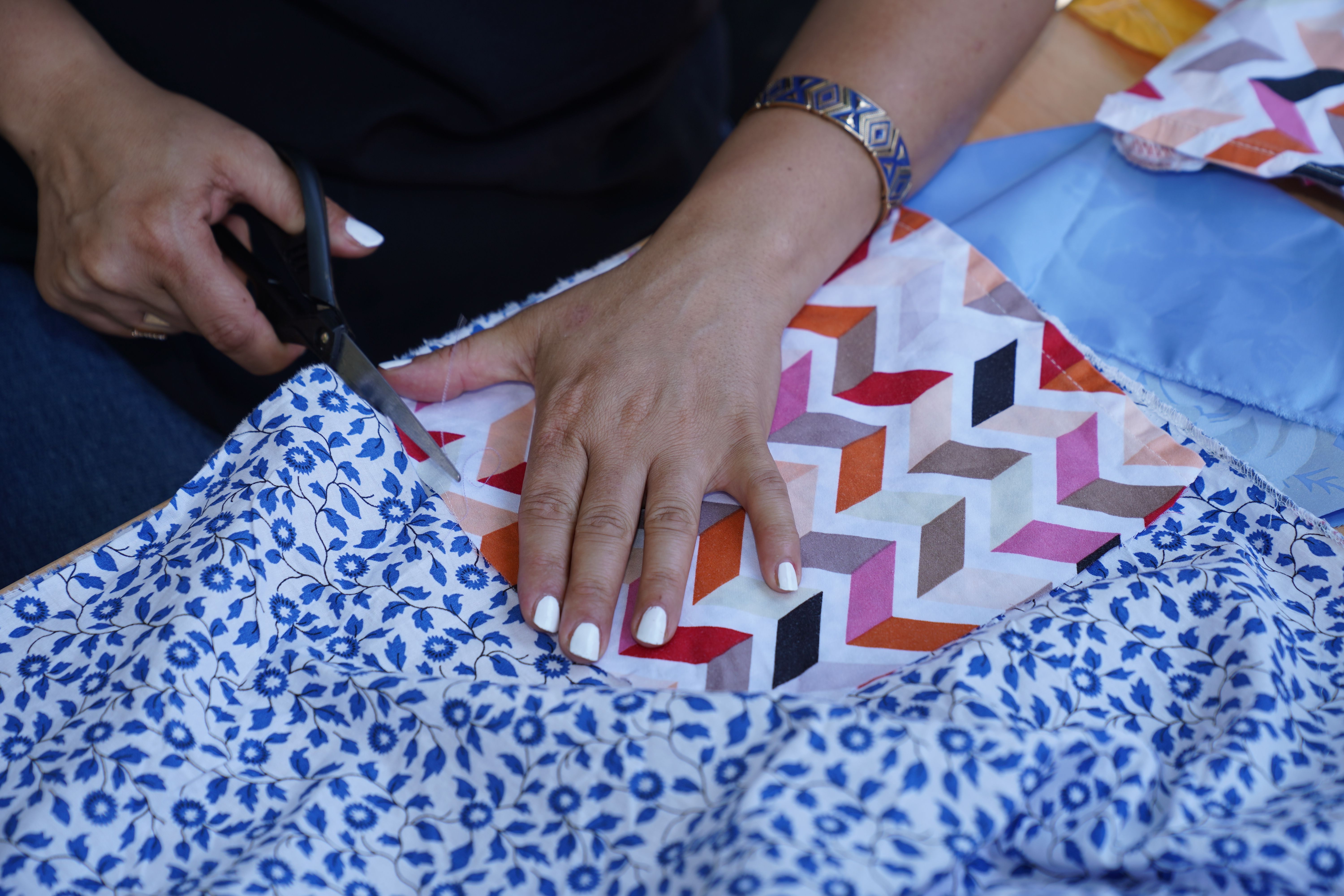 A detailed view of a person cutting colorful fabric with scissors, emphasizing craftsmanship. — Maynard Longarm Quilting