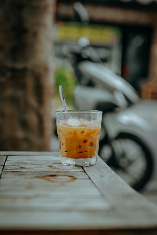 Free Iced coffee on a rustic table with a motorcycle in the background, creating a laid-back vibe. Stock Photo