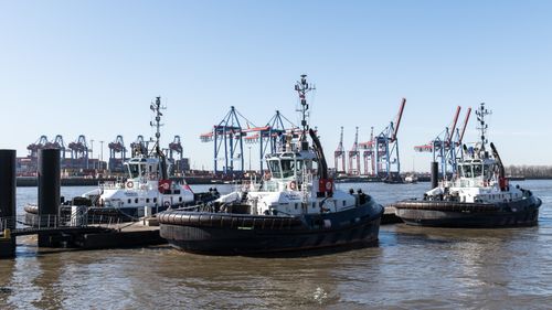 Free Tugboats moored at Hamburg harbor with a backdrop of cranes on a sunny day. Stock Photo