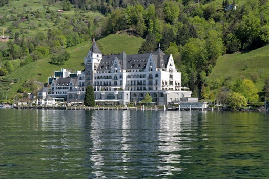 Elegant hotel facade reflecting on a serene Swiss lake with lush green hills in the background.