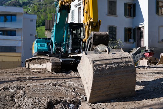 Excavator at a construction site in Vitznau, Switzerland, surrounded by buildings and mountainous terrain.
