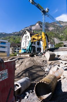 Scenic construction site with a crane and excavator in a Swiss alpine village under clear blue skies.