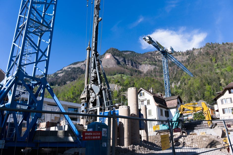 A bustling construction site with cranes against the picturesque Swiss Alps backdrop.