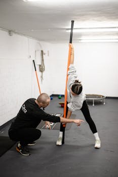 Trainer guides woman through stretching in modern gym setting.