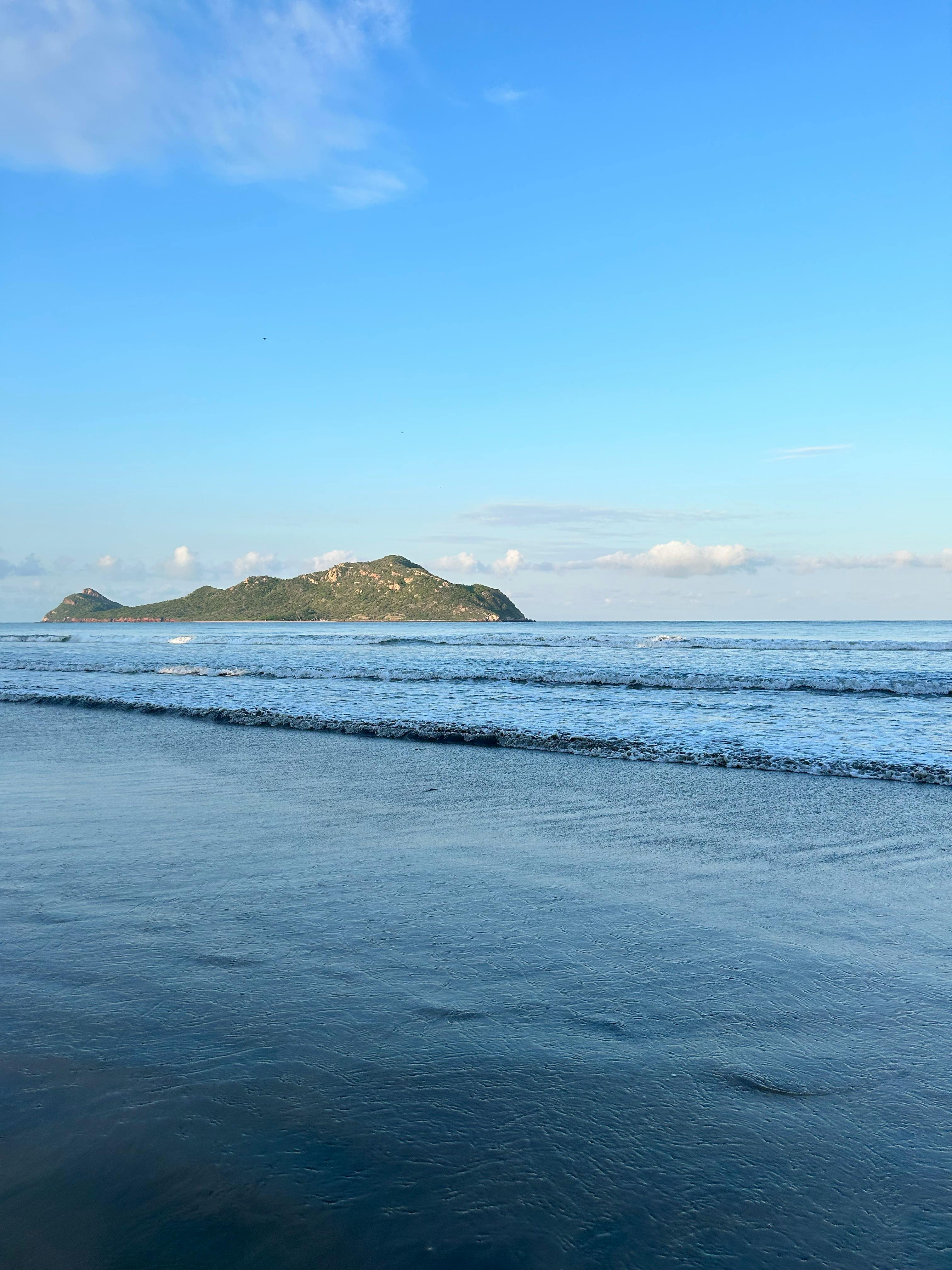 Serene view of Isla Venados from a beach in Mazatlán, capturing the calm ocean and blue sky.