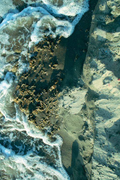 Free An aerial view capturing ocean waves crashing onto a sandy beach with seaweed. Stock Photo