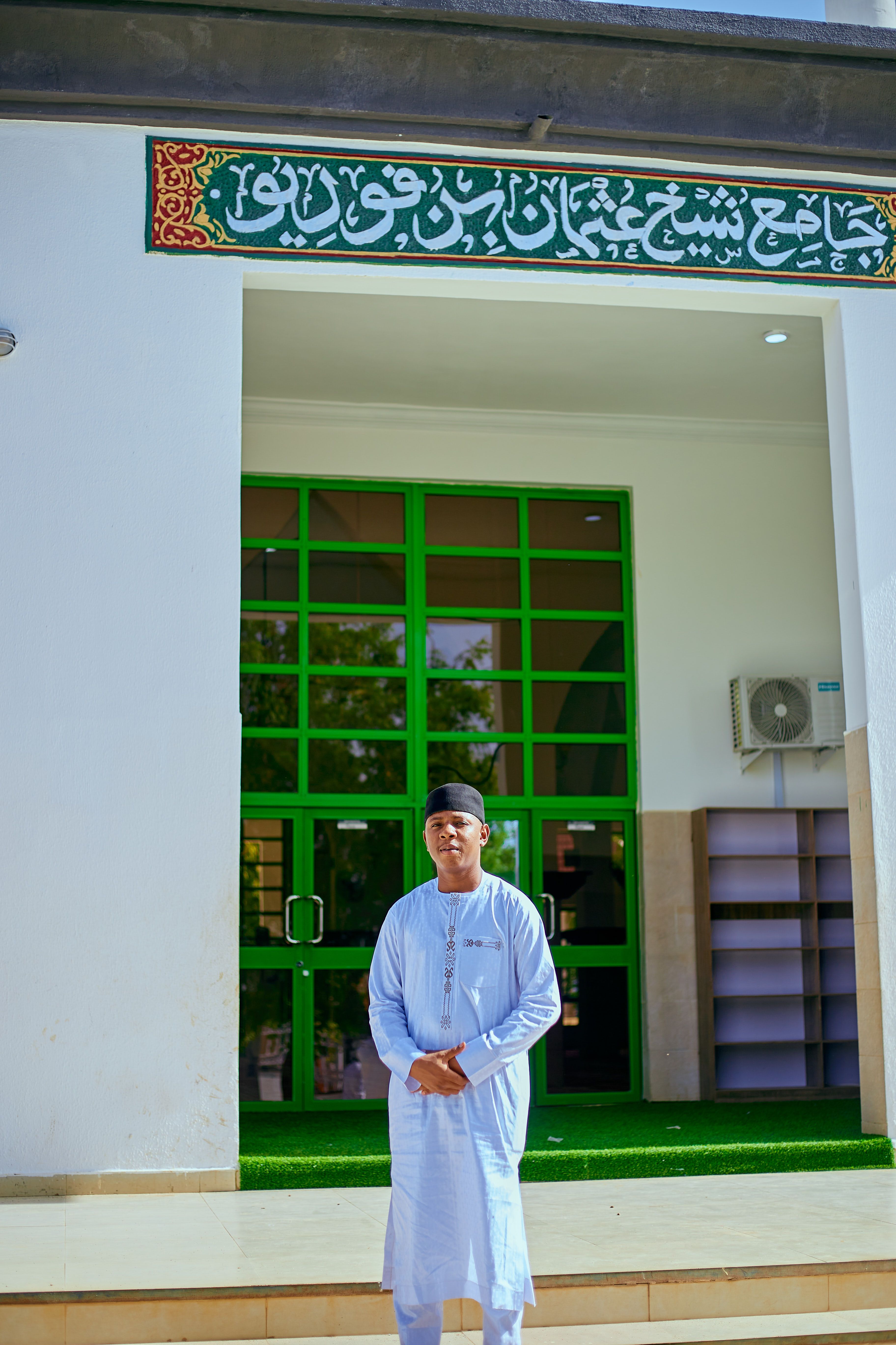 A man in traditional attire stands in front of a mosque entrance, showcasing cultural heritage.