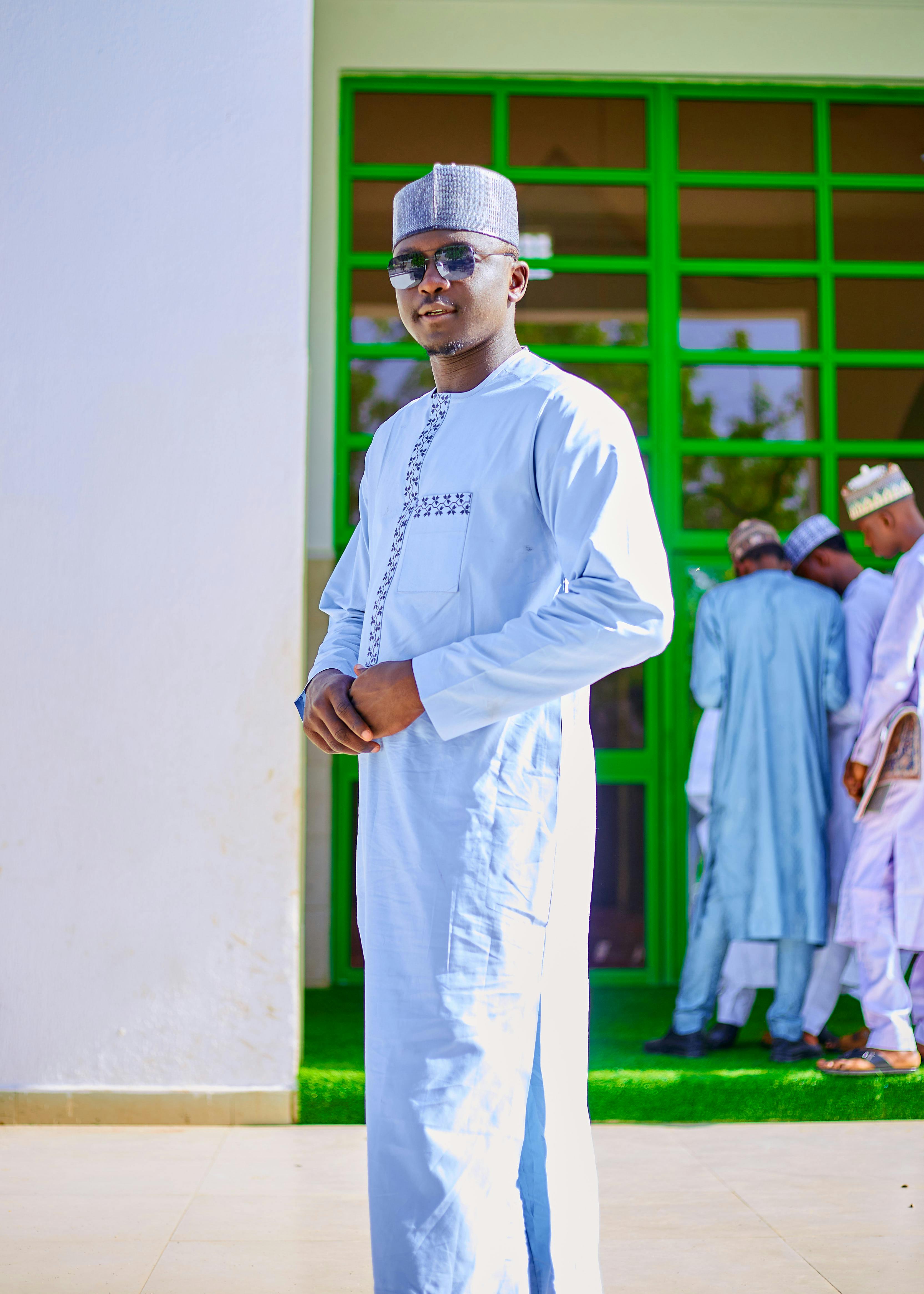 A man in traditional clothing poses confidently, with others in similar attire in the background.