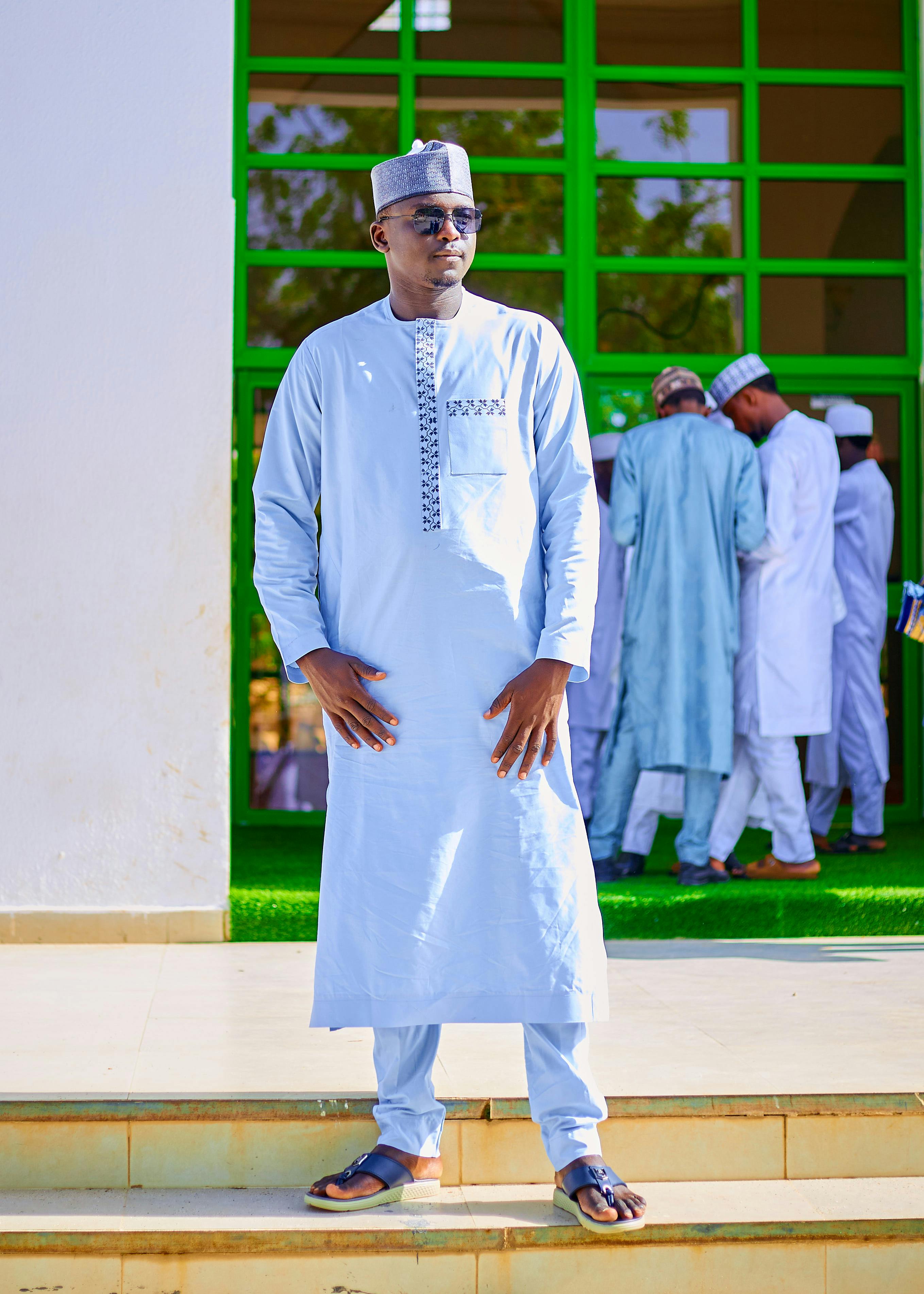 Man posing in traditional attire with group in background outdoors.