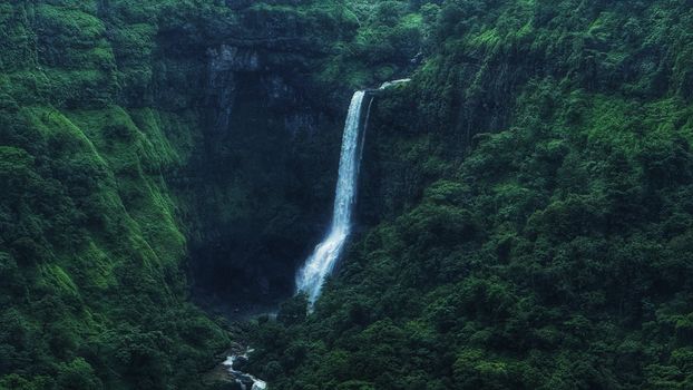 Stunning waterfall amidst dense green forest in serene landscape.