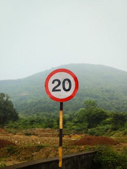 A speed limit sign against a backdrop of lush green hills in Odisha, India, showcasing rural scenery.