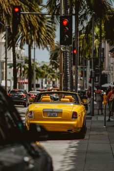 Yellow luxury convertible car on a vibrant, palm-lined street downtown, sunny day.