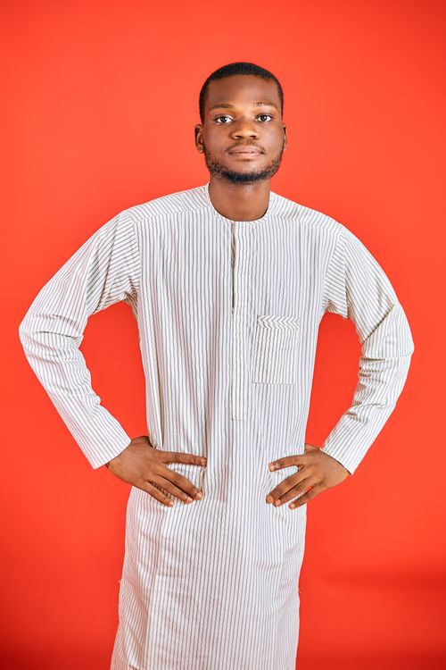 Free Young man posing confidently in striped Nigerian outfit against orange background. Stock Photo