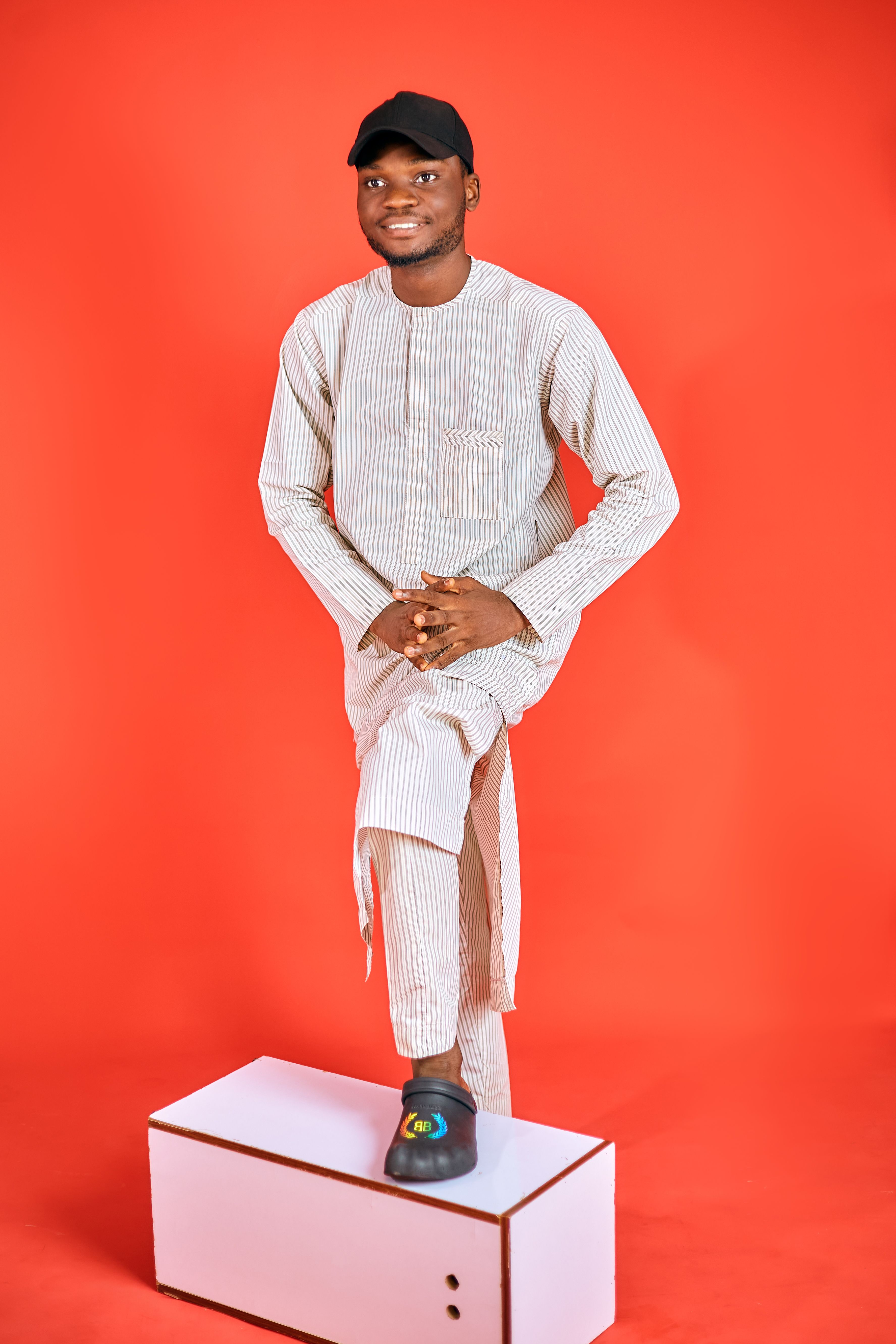 A young man poses confidently in traditional African clothing against a vibrant red background.