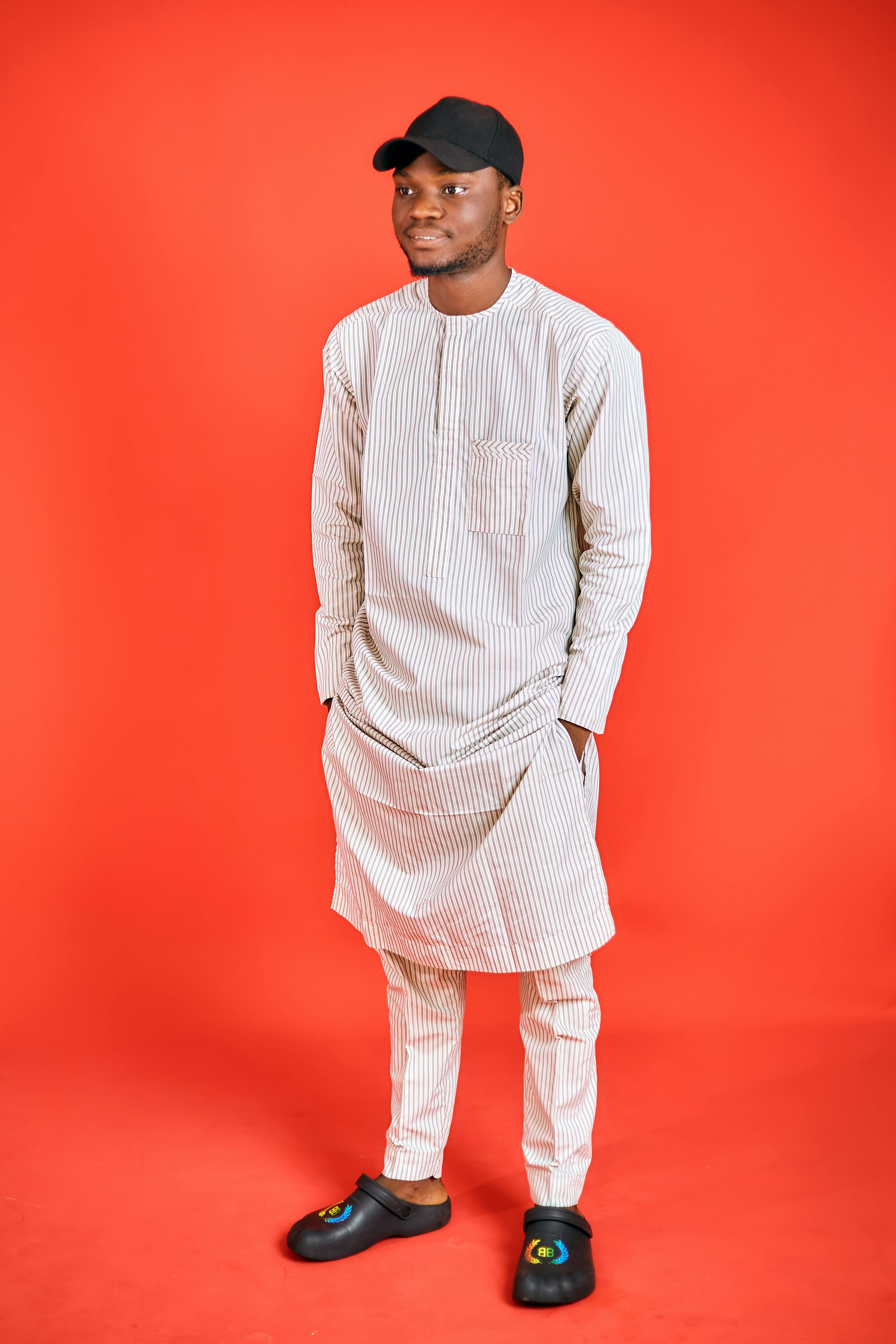 A man in traditional clothing poses against a bold red backdrop in a studio setting.