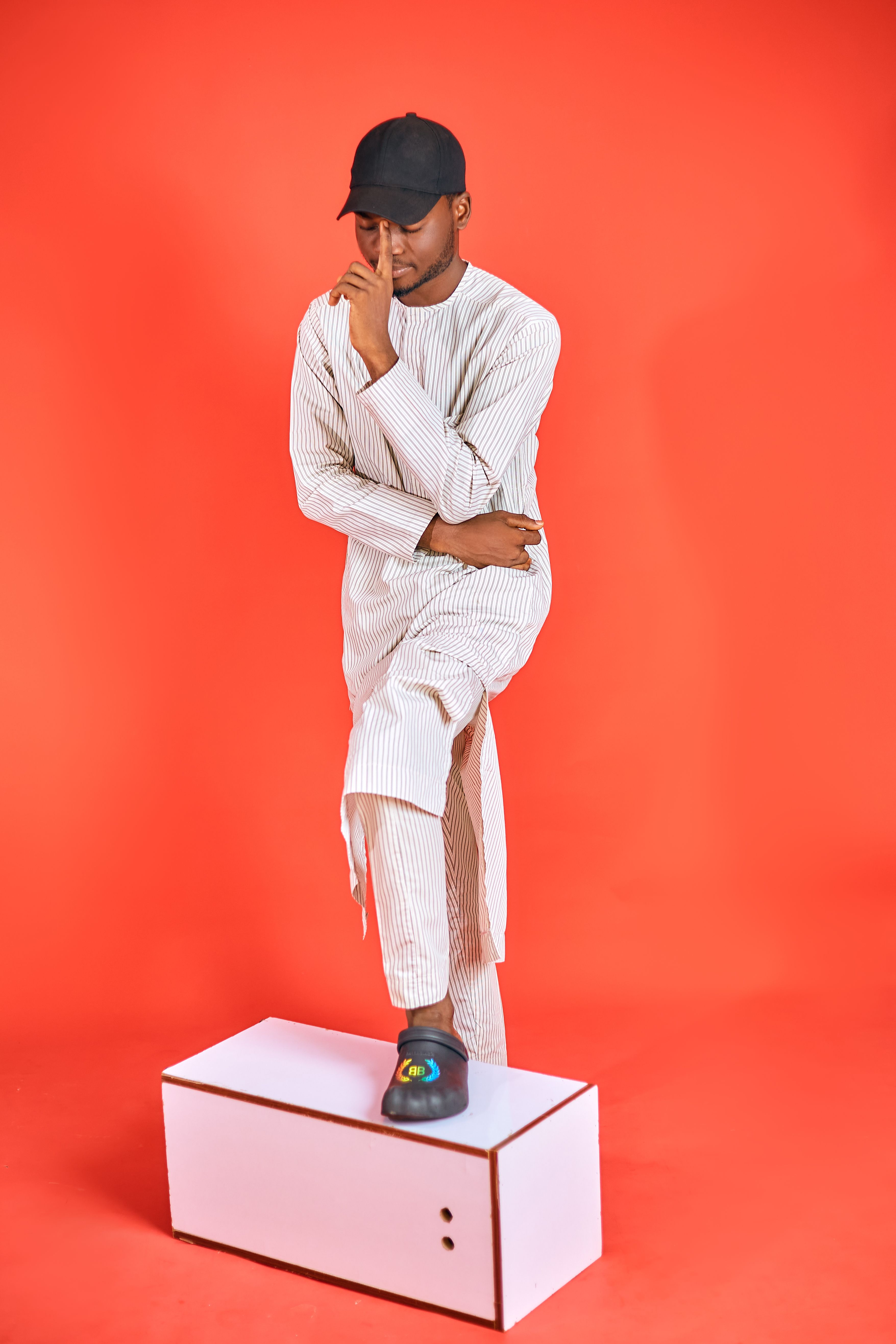 Man posing in traditional attire with a thoughtful expression against a vibrant red background.