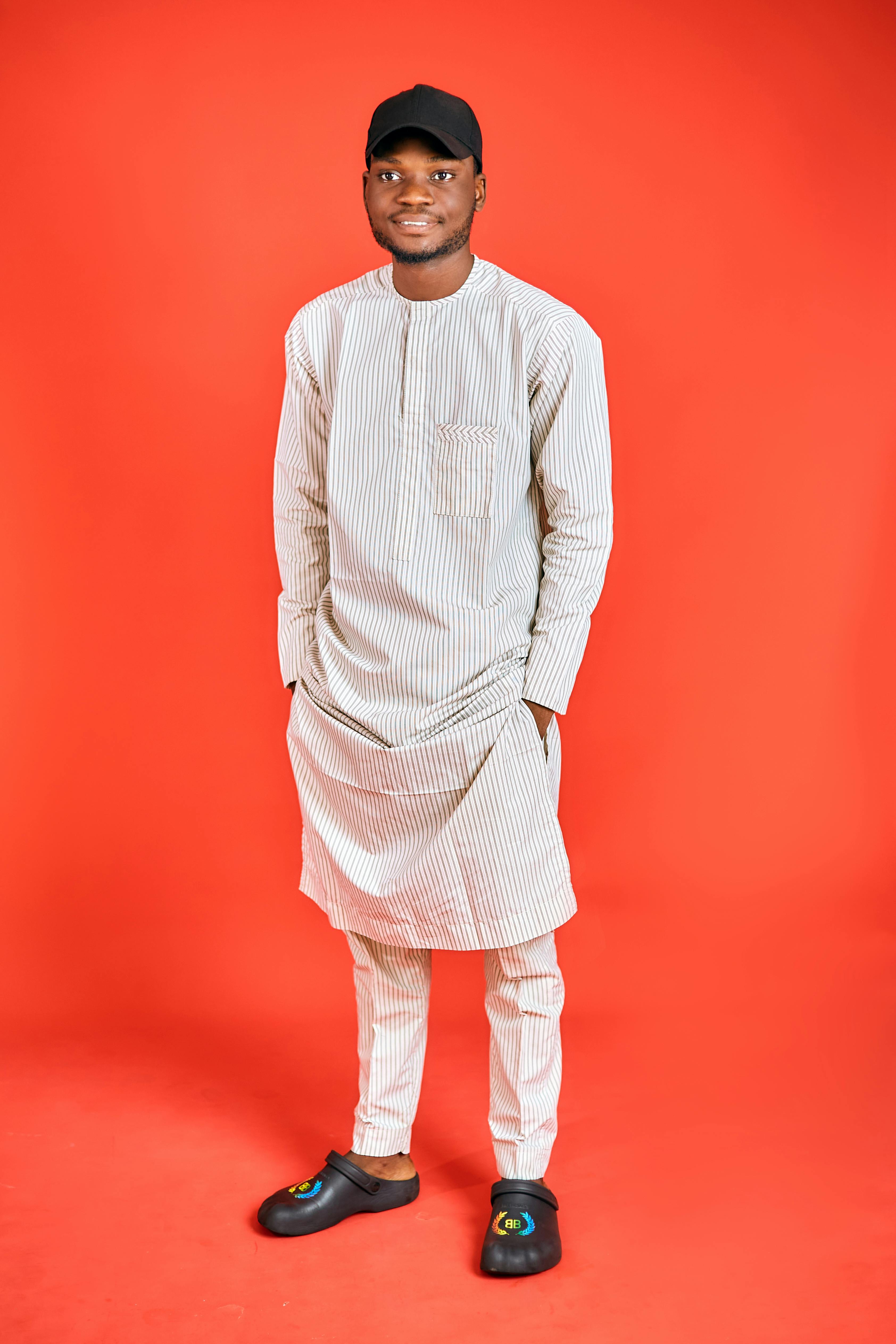 Young adult wearing traditional Nigerian attire posing against a vibrant red background.