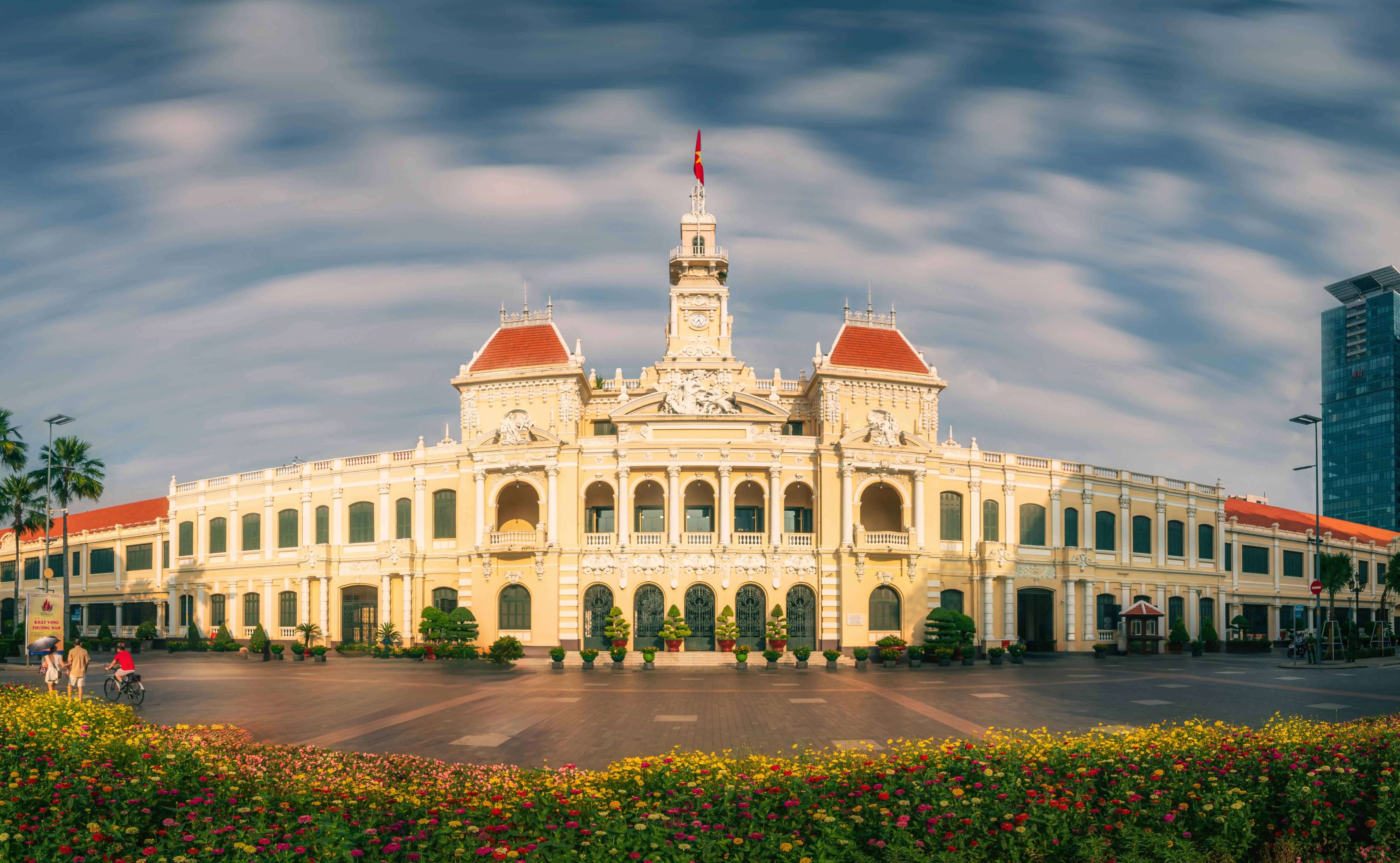 Stunning view of Ho Chi Minh City Hall with vibrant flowers and a dynamic sky, highlighting Vietnamese architecture.