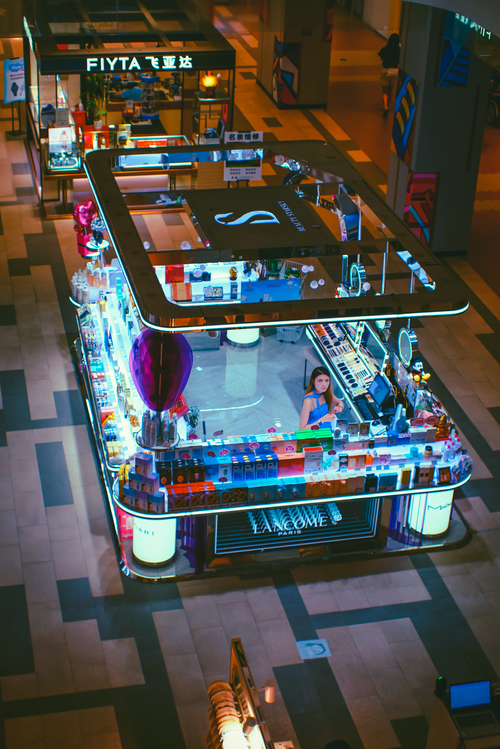 Free A vibrant view of a mall cosmetic kiosk showcasing products with a central salesperson. Stock Photo